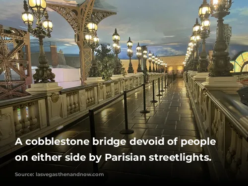 A cobblestone bridge devoid of people lined on either side by Parisian streetlights. 