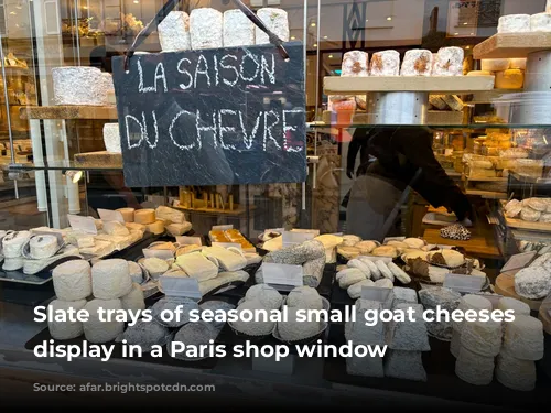 Slate trays of seasonal small goat cheeses on display in a Paris shop window