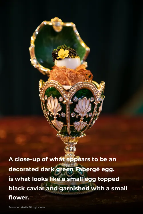 A close-up of what appears to be an ornately decorated dark green Fabergé egg. Inside is what looks like a small egg topped with black caviar and garnished with a small yellow flower. 