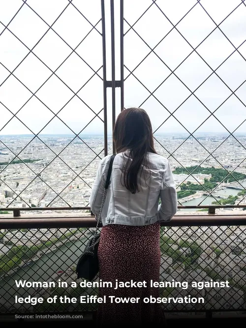 Woman in a denim jacket leaning against the ledge of the Eiffel Tower observation deck