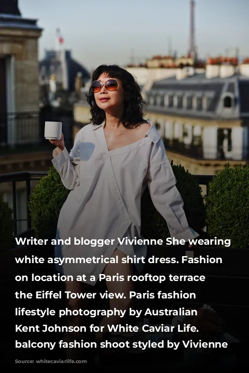 Writer and blogger Vivienne She wearing a white asymmetrical shirt dress. Fashion portraits on location at a Paris rooftop terrace with the Eiffel Tower view. Paris fashion and lifestyle photography by Australian photographer Kent Johnson for White Caviar Life. Paris balcony fashion shoot styled by Vivienne She.