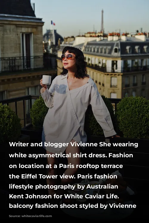 Writer and blogger Vivienne She wearing a white asymmetrical shirt dress. Fashion portraits on location at a Paris rooftop terrace with the Eiffel Tower view. Paris fashion and lifestyle photography by Australian photographer Kent Johnson for White Caviar Life. Paris balcony fashion shoot styled by Vivienne She.