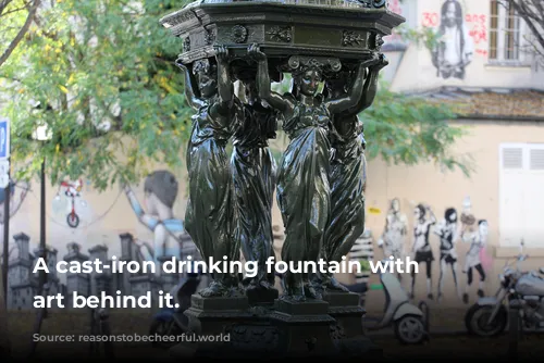 A cast-iron drinking fountain with street art behind it.