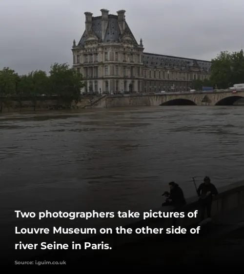 Two photographers take pictures of the Louvre Museum on the other side of the river Seine in Paris.