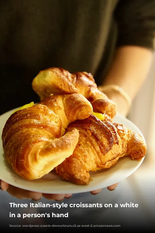 Three Italian-style croissants on a white plate in a person's hand