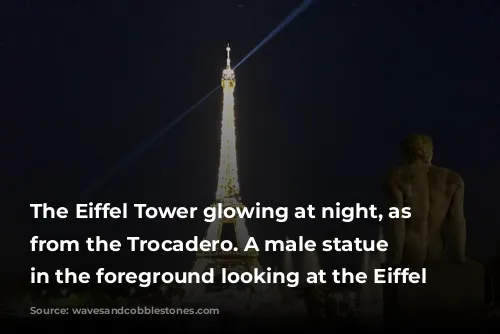 The Eiffel Tower glowing at night, as seen from the Trocadero.  A male statue is in the foreground looking at the Eiffel Tower.