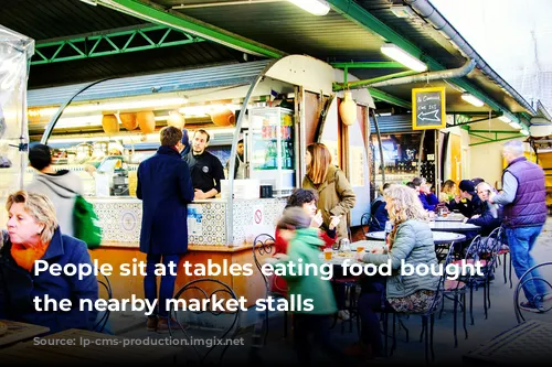 People sit at tables eating food bought from the nearby market stalls