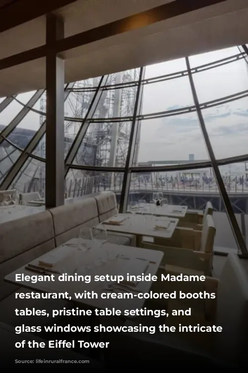 Elegant dining setup inside Madame Brasserie restaurant, with cream-colored booths and tables, pristine table settings, and large glass windows showcasing the intricate metalwork of the Eiffel Tower