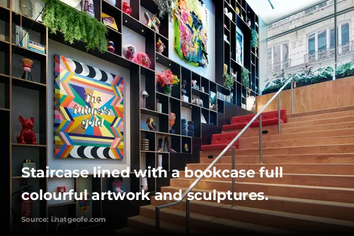 Staircase lined with a bookcase full of colourful artwork and sculptures.