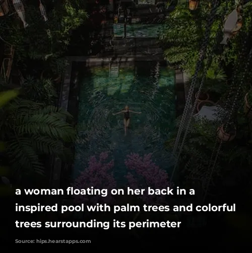 a woman floating on her back in a bali inspired pool with palm trees and colorful flowering trees surrounding its perimeter