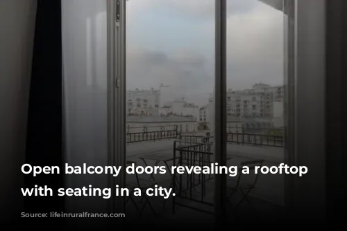 Open balcony doors revealing a rooftop patio with seating in a city.